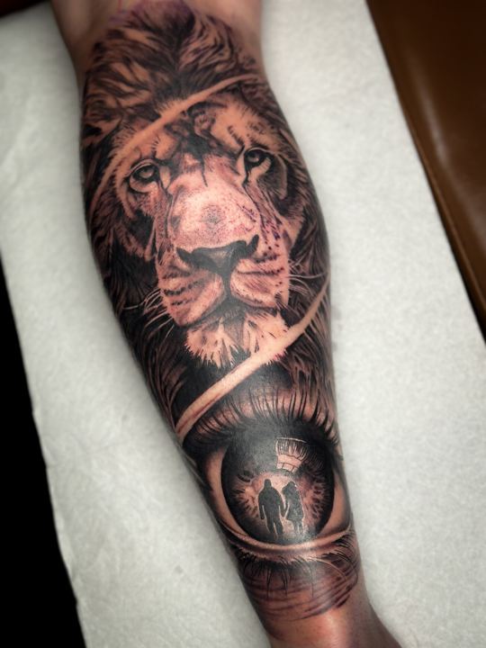 Black and grey realism lion and eye tattoo on a forearm