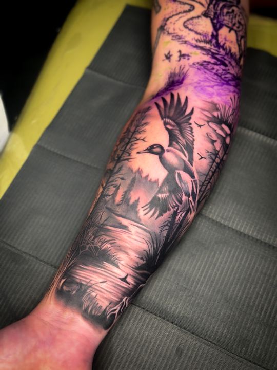 Black and grey realism duck and marsh landscape on a forearm